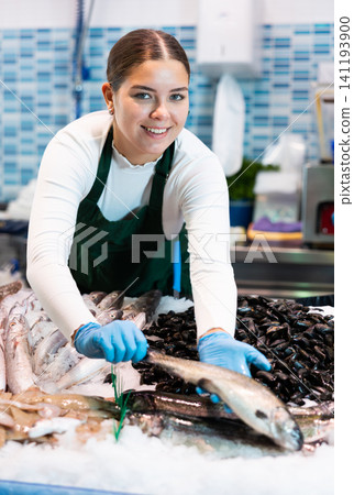 Positive saleswoman demonstrating trout in fish store Positive saleswoman demonstrating trout in fish store 141193900