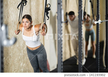 Girl trains on gymnastic rings in modern crossfit gym 141193902