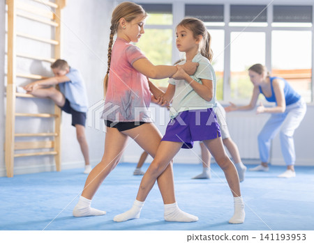 Boys and girls in gym perform basic elements of krav maga self-defense system. Boys and girls in gym perform basic elements of krav maga self-defense system. 141193953