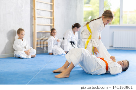 Children in white kimono training judo, jiu-jitsu indoors. Professional sports club for kids. Concept of martial arts, combat sport, sport education, childhood, hobby Children in white kimono training judo, jiu-jitsu indoors. Professional sports club for kids. Concept of martial arts, combat sport, sport education, childhood, hobby 141193961