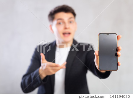 Surprised young guy holding mobile phone in his hand Surprised young guy holding mobile phone in his hand 141194020
