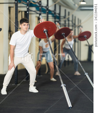 Athletic young guy pumping up her arm biceps using one side of barbell Athletic young guy pumping up her arm biceps using one side of barbell 141194051