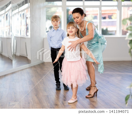 Female dance teacher adjusting stance of preteen girl rehearsing curtsey Female dance teacher adjusting stance of preteen girl rehearsing curtsey 141194071