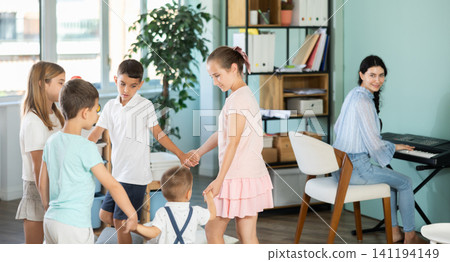 Children dancing in circle while teacher plays music on synthesizer Children dancing in circle while teacher plays music on synthesizer 141194149