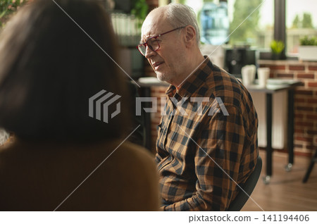 Elderly man speaks about addiction recovery in a brick wall support group, sharing progress, guidance and emotional help during a therapy meeting. Elderly man speaks about addiction recovery in a brick wall support group, sharing progress, guidance and emotional help during a therapy meeting. 141194406