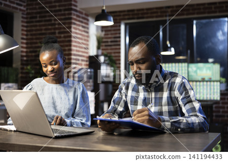 Coworkers discuss stock figures in nighttime office during a office setting moment involving african american, real time and tech savvy 141194433