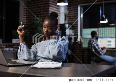 Exhausted trading employee sits at a desk with neck pain while reviewing investor portfolio data, charts and market information late at work, with the action centered on financial, market and a. Exhausted trading employee sits at a desk with neck pain while reviewing investor portfolio data, charts and market information late at work, with the action centered on financial, market and a. 141194475