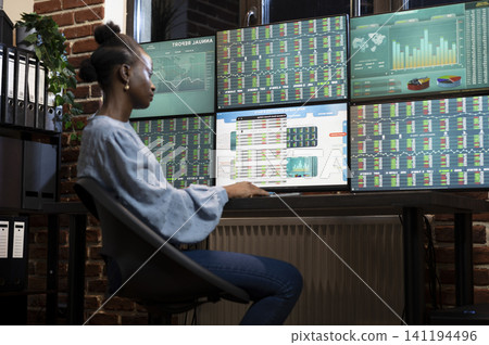 Forex trader analyzes market growth on multiple monitors, using keyboard work, financial trends and stock charts in a brick office. Forex trader analyzes market growth on multiple monitors, using keyboard work, financial trends and stock charts in a brick office. 141194496
