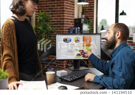 Businessman explains marketing strategy and company data charts to a woman manager during focused planning work in a startup office. Businessman explains marketing strategy and company data charts to a woman manager during focused planning work in a startup office. 141194510