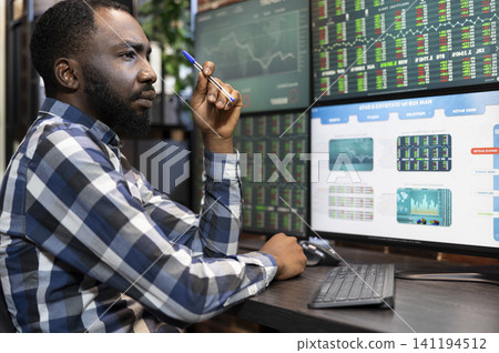 Focused stockbroker works late at a desk, reviewing stock market data, trading statistics and charts across multiple office monitors, as a broker workstation and investment concept. Focused stockbroker works late at a desk, reviewing stock market data, trading statistics and charts across multiple office monitors, as a broker workstation and investment concept. 141194512