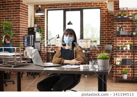 Confident businesswoman poses at a desk with laptop and financial documents, showing startup workspace, professional portrait and office work. Confident businesswoman poses at a desk with laptop and financial documents, showing startup workspace, professional portrait and office work. 141194513