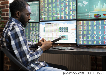 Stock manager writes progress updates on a clipboard for a hedge fund, connecting risk analysis and stock trading work in an office. Stock manager writes progress updates on a clipboard for a hedge fund, connecting risk analysis and stock trading work in an office. 141194539