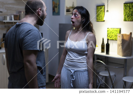 Husband and wife shout at each other during an aggressive domestic dispute, showing social problems, intimidation and violence inside a conflicted home. 141194577