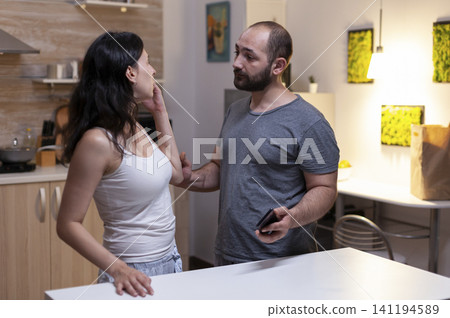 Husband holding smartphone from wife with secret messages arguing because of jealousy and infidelity, irritated woman with lover caught cheating at home. Husband holding smartphone from wife with secret messages arguing because of jealousy and infidelity, irritated woman with lover caught cheating at home. 141194589