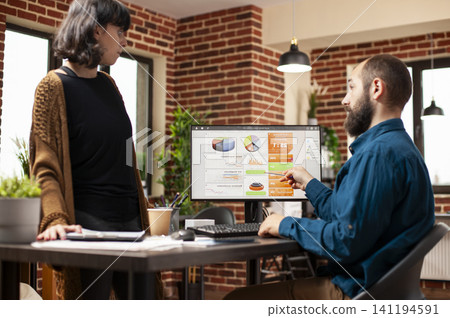 Male manager discusses a company research presentation with a female employee on a desktop monitor while planning a business project in the office. Male manager discusses a company research presentation with a female employee on a desktop monitor while planning a business project in the office. 141194591