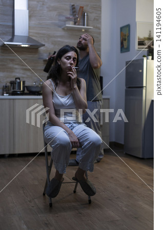 Unhappy bruised woman smokes in a kitchen after domestic violence, reflecting misery, physical abuse and harassment from a violent drunk husband. 141194605