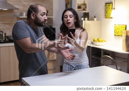 Jealous wife catches her husband checking secret smartphone messages, showing infidelity suspicion, yelling, trust issues and marriage conflict. Jealous wife catches her husband checking secret smartphone messages, showing infidelity suspicion, yelling, trust issues and marriage conflict. 141194620