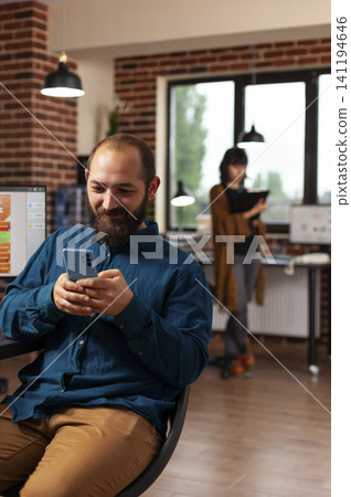 Businessman in a startup office browses a smartphone for social media messages and online information while developing remote communication ideas. Businessman in a startup office browses a smartphone for social media messages and online information while developing remote communication ideas. 141194646