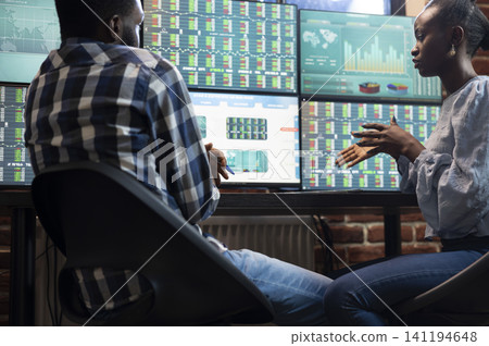 Colleagues analyzing stock charts at desk presenting focused male and female colleagues at desk, analyzing real time stock market charts on multiple monitors in a modern office. Colleagues analyzing stock charts at desk presenting focused male and female colleagues at desk, analyzing real time stock market charts on multiple monitors in a modern office. 141194648
