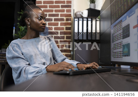 Businesswoman monitoring forex charts late at night featuring focused black businesswoman staying up late at her desk, monitoring forex trading charts on several screens. Businesswoman monitoring forex charts late at night featuring focused black businesswoman staying up late at her desk, monitoring forex trading charts on several screens. 141194656