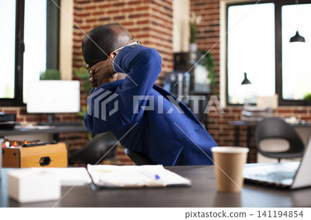 Entrepreneur stretches his back in a startup office after completing tasks, showing satisfaction and recovery during a productive work session. Entrepreneur stretches his back in a startup office after completing tasks, showing satisfaction and recovery during a productive work session. 141194854