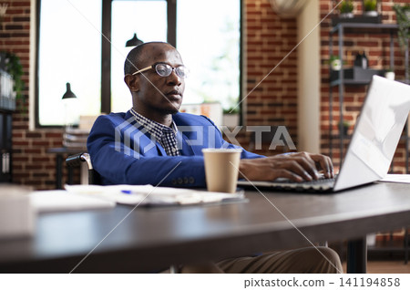 Black entrepreneur in a wheelchair uses a laptop at an office desk, reviewing business plans and financial ideas for company management. Black entrepreneur in a wheelchair uses a laptop at an office desk, reviewing business plans and financial ideas for company management. 141194858