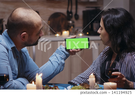 Married young couple holds a smartphone mockup at dinner, using a green screen display template for editable mobile content, during a digital dinner moment. Married young couple holds a smartphone mockup at dinner, using a green screen display template for editable mobile content, during a digital dinner moment. 141194925