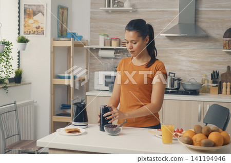 Cheerful wife grinds coffee beans for breakfast during a morning kitchen routine, combining coffee grinder, coffee beans and ground coffee for food and beverage lifestyle content. Cheerful wife grinds coffee beans for breakfast during a morning kitchen routine, combining coffee grinder, coffee beans and ground coffee for food and beverage lifestyle content. 141194946
