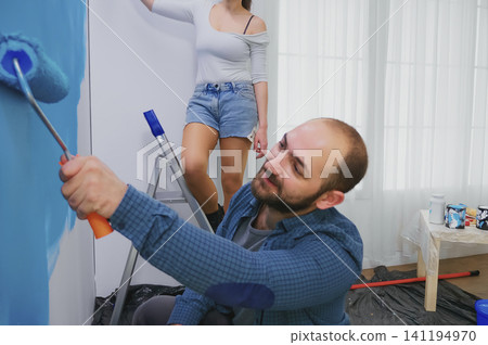 Wife paints apartment wall from ladder as a wife paints a wall from a ladder during home repair, apartment makeover and redecorating work. Wife paints apartment wall from ladder as a wife paints a wall from a ladder during home repair, apartment makeover and redecorating work. 141194970