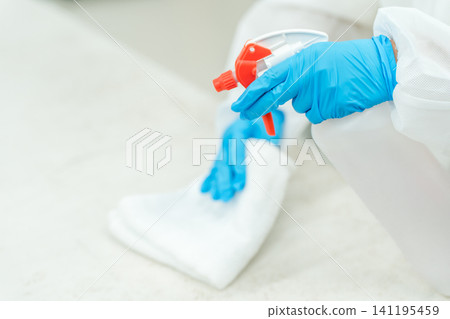 用消毒噴霧和酒精消毒水擦拭桌子，雙手戴著丁腈手套。 141195459