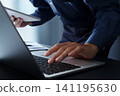 A businessman using a computer at his desk and looking at a tablet PC. Close-up of his hands and keyboard. Business tech 141195630