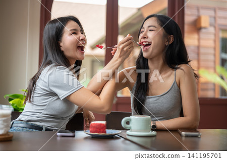 Asian women friends sharing a cake and laughter during coffee time in bright modern cafe with warmth Asian women friends sharing a cake and laughter during coffee time in bright modern cafe with warmth 141195701