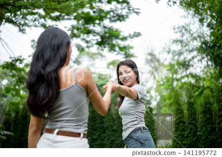Beautiful Asian woman holding hands and pulling her friend to dance in the garden. Beautiful Asian woman holding hands and pulling her friend to dance in the garden. 141195772