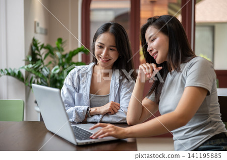 Smiling Asian woman typing on laptop while working with her teammate in cafe. Smiling Asian woman typing on laptop while working with her teammate in cafe. 141195885