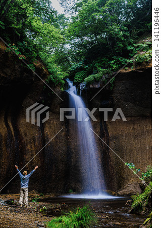 A man stands before the Shichijo Falls in summer, arms outstretched, soaking up the power of nature with his whole body. A man stands before the Shichijo Falls in summer, arms outstretched, soaking up the power of nature with his whole body. 141196446