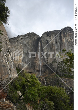 Low-angle view of Upper Yosemite Fall cascading down towering granite cliffs. Low-angle view of Upper Yosemite Fall cascading down towering granite cliffs. 141196603