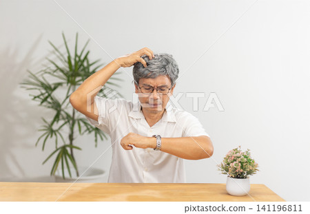 Senior Asian man with dementia struggles to set the time and day on his watch. Senior Asian man with dementia struggles to set the time and day on his watch. 141196811