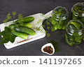 Cucumbers in glass jars and on a cutting board, dill, garlic, and spices on a white wooden background.  141197265