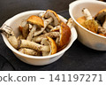 Fresh mushrooms are gathered in two bowls placed on a dark kitchen countertop.  141197271
