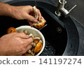 Water runs from a faucet as a person washes mushrooms in a bowl.  141197274