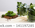Cucumbers in glass jars and on a cutting board, dill, garlic, and spices on a white wooden background.  141197285