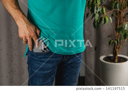 Man reaches for smartphone in pocket of jeans while standing indoors 141197515