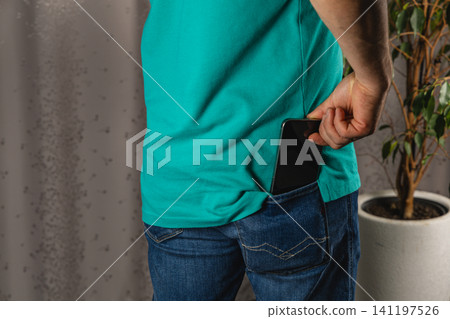 A man is placing his smartphone into the pocket of his denim jeans A man is placing his smartphone into the pocket of his denim jeans 141197526