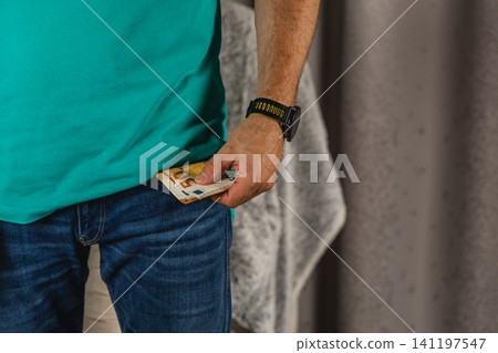 Man places euro money in pocket of blue jeans while standing indoors 141197547