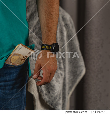 Man with money in jeans pocket standing by a gray background Man with money in jeans pocket standing by a gray background 141197550