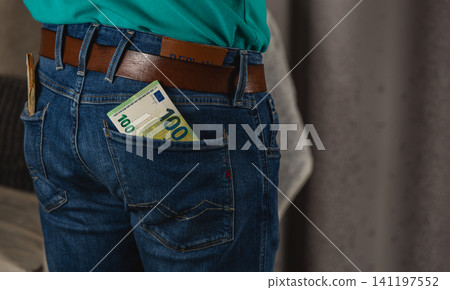 Man standing with money in the back pocket of blue jeans in a modern setting Man standing with money in the back pocket of blue jeans in a modern setting 141197552