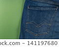 Closeup of a denim pocket on jeans against a green background 141197680