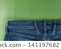 Casual blue denim jeans with pockets and zipper detail on a green background 141197682
