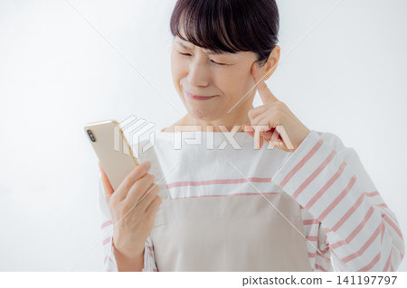 一位家庭主婦看著她的智慧型手機,憂心忡忡。 一位家庭主婦看著她的智慧型手機,憂心忡忡。 141197797