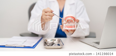 Dentist with Orthodontic tooth model and bracket or brace. Clean and Scrape off tartar. May Orthodontic Health Day, March Oral health, Dentist Day, False Teeth. Toothache and Children Dental Health Dentist with Orthodontic tooth model and bracket or brace. Clean and Scrape off tartar. May Orthodontic Health Day, March Oral health, Dentist Day, False Teeth. Toothache and Children Dental Health 141198014
